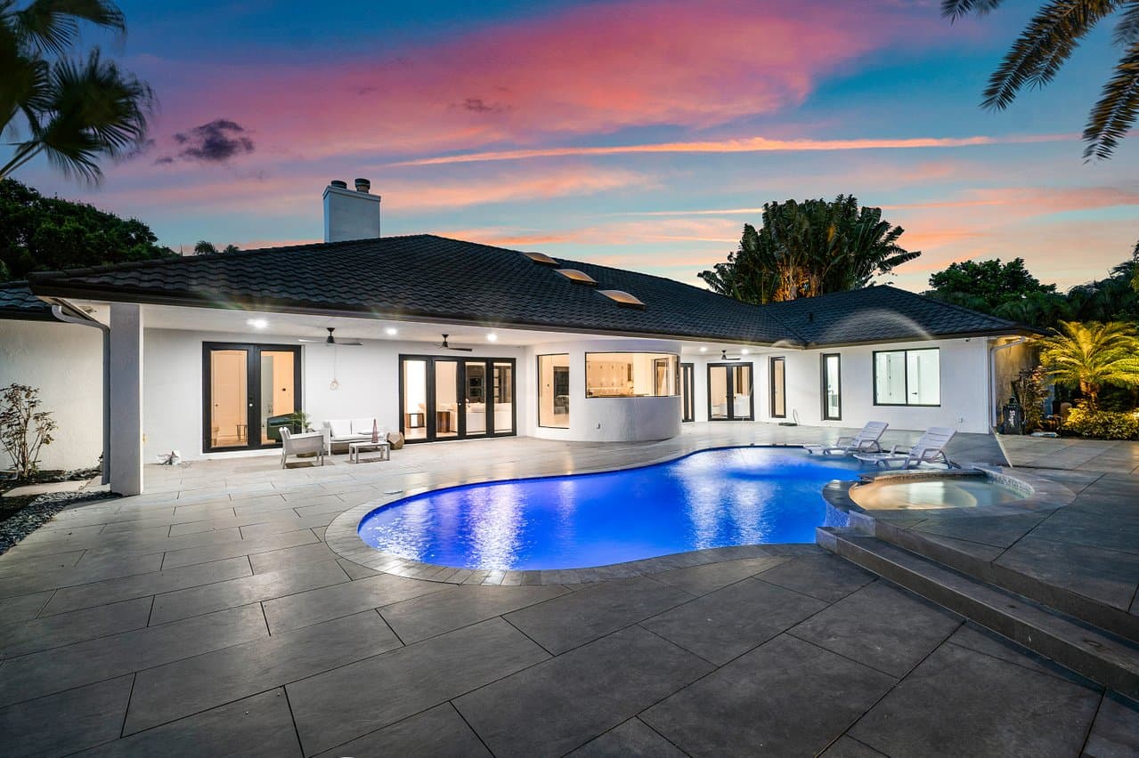 Pool home rear elevation with impact sliders and French doors at dusk